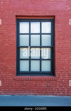 Zwölf Fenster mit schwarzem Rahmen und Milchglas in einer alten, rot gestrichenen Ziegelwand. Stockfoto