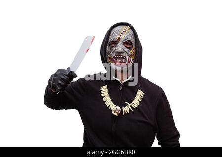 Ein Mann, der in einer Zombie-Maske verkleidet ist und ein schwarzes Kapuzen-Sweatshirt und Handschuhe trägt, droht mit einem blutigen Schlachtermesser. Stockfoto