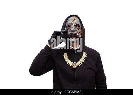 Ein Mann, der in einer Zombie-Maske gekleidet ist und ein schwarzes Kapuzen-Sweatshirt trägt, frisst eine Spielzeug-Spinne. Stockfoto