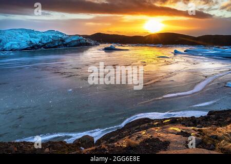 Der Svinafellsjokul-Gletscher in Island und die gefrorene Gletscherlagune bei Sonnenuntergang. Die niedrige Sonne scheint auf dem Ufer, wodurch die Eisablagerungen Gold glänzen. Wi Stockfoto