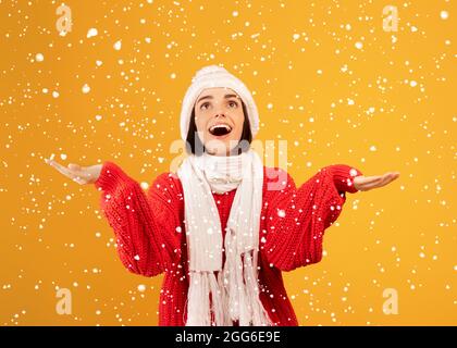 Der Winter ist gekommen. Glückliche Frau im Winter Hut und Schal spielen mit Schneeflocken, posiert auf gelbem Hintergrund Stockfoto