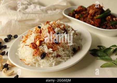 Reisgericht aus Basmati-Reis, Ghee und Gewürzen und garniert mit gebratenen Zwiebeln serviert mit Kerala Stil würzigen Hähnchenbraten. Eine beliebte Mahlzeit kombiniert Stockfoto