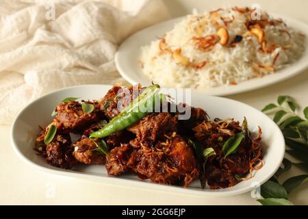 Würziger Hähnchenbraten im Kerala-Stil, serviert mit Ghee-Reis aus Basmati-Reis, garniert mit gebratenen Zwiebeln und Cashews. Eine beliebte Kombination aus Speisen Stockfoto