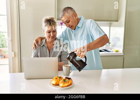Ein älteres kaukasisches Paar, das mit einem Laptop in der Küche frühstückte. Stockfoto