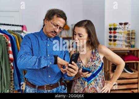 Interrassisches Paar im mittleren Alter im Einzelhandel mit Smartphone, das die Zeit auf der Armbanduhr überprüft, entspannt und selbstbewusst Stockfoto