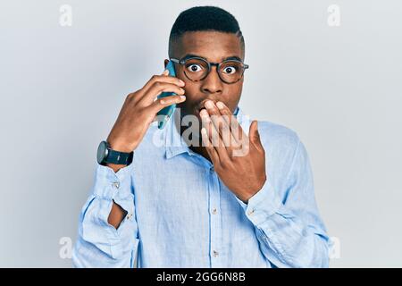 Junger afroamerikanischer Mann mit Gespräch Gespräch auf dem Smartphone über den Mund mit der Hand, schockiert und Angst vor Fehler. Überrascht expressio Stockfoto
