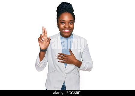 Junge afroamerikanische Frau in Geschäftskleidung lächelnd, mit der Hand auf der Brust und den Fingern nach oben verfluchend, einen Treueversprechen-Eid abmachend Stockfoto