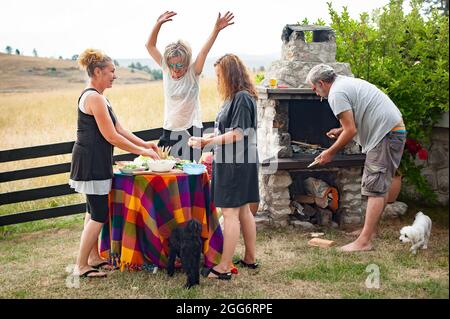 Fröhliche und verspielte Freunde lachen, tanzen und genießen das Bergambiente und grillen vor ihrem Haus Stockfoto