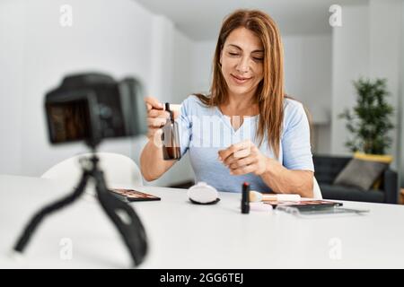 Kaukasische Frau mittleren Alters macht Make-up-Tutorial mit Kamera sitzen auf dem Tisch zu Hause. Stockfoto