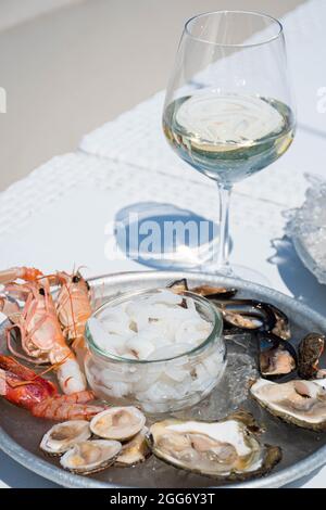 Teller mit rohen frischen Meeresfrüchten oder Lebensmitteln, verzehrfertig mit Garnelen, Garnelen, Austern, Muscheln, Muscheln, Muscheln, Tintenfisch mit Glas Weißwein, vertikal Stockfoto