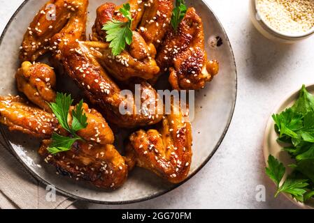 Teriyaki Hähnchenflügel mit Sesam und Grüns auf weißem Hintergrund aus nächster Nähe. Asiatisches Gericht: Gebratene Hähnchenflügel mit Teriyaki-Sauce. Stockfoto