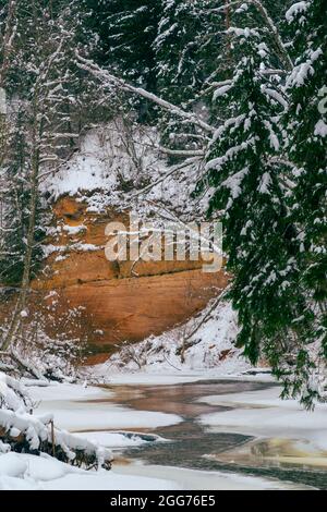 Der Fluss Rauna ist gefroren und mit Schnee bedeckt, und die Klippen von Raibās sind in der Ferne zu sehen. In der Mitte des Flusses sehen wir einen schmalen Streifen o Stockfoto