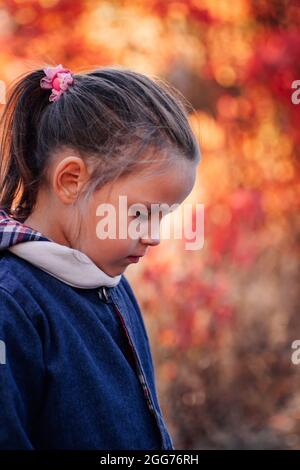 Seitenansicht Mädchen Porträt. Schöne kleine Mädchen in blauen Jeans Jacke Blick nach unten auf Herbst Wald Hintergrund Stockfoto