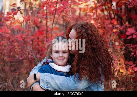 Nahaufnahme glücklich Familie Konzept. Mutter mit langen kurvigen Haaren Kuss lächelndes Mädchen auf Herbst Wald Hintergrund. Glückliche Mutterschaft Stockfoto