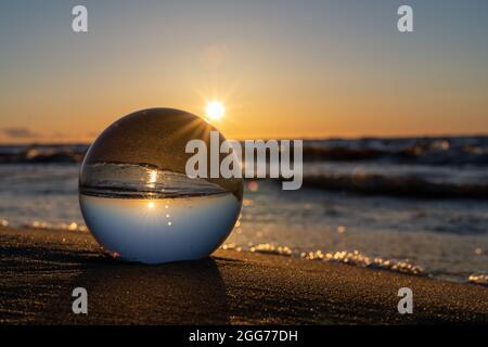 Die Glaskugel befindet sich an der sandigen Küste zwischen dem Strand und den Meereswellen Stockfoto