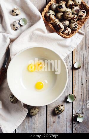 Zerbrochene Wachteleier in einer Schüssel auf einem hölzernen Hintergrund. Stockfoto