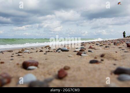 Kleine Kieselsteine verstreut auf dem Strand Sand Nahaufnahme.niedrige Schärfentiefe.Selektive Fokus auf die Vordergrundsteine.EIN verschwommener Hintergrund von bunten sto Stockfoto