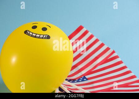 Gelbe Emoji-Ballons mit amerikanischen Flaggen auf blauem Hintergrund. Stockfoto