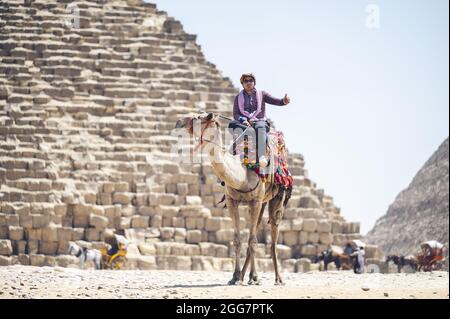 KAIRO, ÄGYPTEN - 06. Jun 2021: Ein Tourist, der in Ca, Ägypten, auf einem Kamel gegen eine alte Pyramide reitet Stockfoto