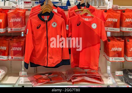 tokio, japan - 24 2021. august: Offizielles orangefarbenes Fans-T-Shirt und Podestjacke der Olympischen Spiele und Paralympics-Teams in Japan, geschmückt mit fünf ri Stockfoto