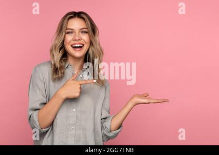 Aufgeregt junge Frau zeigen Finger auf offene Handfläche für neue Produkte oder Verkauf. Überglücklich glücklich blonde Mädchen Stockfoto