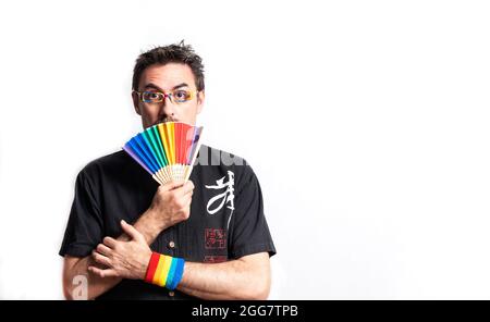 Dunkelhaariger Mann in einem schwarzen Hemd mit Brille und einem regenbogenfarbenen Armband; mit einem überraschten Gesicht bedeckt er seinen Mund mit einem regenbogenfarbenen fa Stockfoto