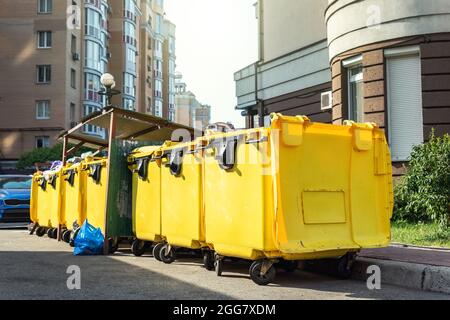 Reihen von vielen großen gelben Plastikmüllbehältern voller schwarzer Plastikmüllbeutel in der Nähe von Wohngebäuden in der Innenstadt oder im Vorstadtbereich. Nicht Stockfoto