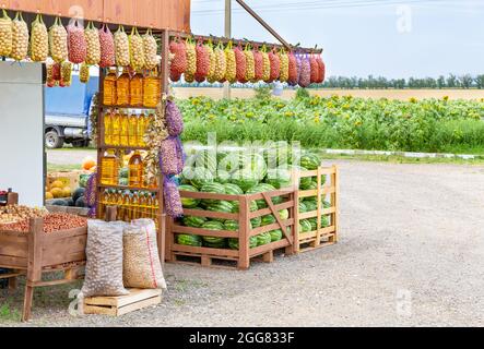 Straßenlandwirte verkaufen Bio-Öko-Lebensmittel vor dem Hintergrund eines Feldes mit Sonnenblumen. Pflanzenöl in Flaschen, Kartoffeln in Netzen Stockfoto