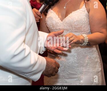 Ehemann und Ehefrau reichen ihren neuen Diamanten während der Hochzeit an den Ringfinger. Stockfoto