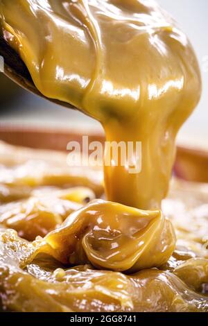 dulce de leche oder hausgemachtes Karamell tropft aus Holzlöffel, Makro-Foto von Lebensmitteln Stockfoto