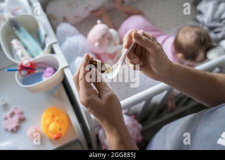 Vater bereitet Löffel mit probiotischen Tropfen Medizin für sein kleines kaukasisches Baby Mädchen, während er bei der Wiege Krippe zu Hause aus der Nähe auf Hände Sel stehen Stockfoto
