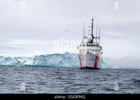 LABRADOR SEA -- (Aug 19, 2021) die USCGC Escanaba (WMEC 907) durchfährt einen Eisberg in der Labradorsee. Die Escanaba ist ein 270 Meter langer, berühmter Mittelausdauerschneider mit einer Besatzung von rund 100 Personen und führt Missionen durch, die die Sicherheit im Seeverkehr und die Strafverfolgung (US Foto der Küstenwache von Petty Officer, 3. Klasse, Dyxan Williams.) Stockfoto