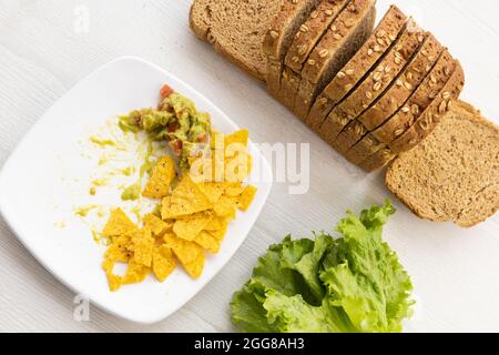 Auf einem Tisch eine Form von geschnittenem Vollkornbrot neben einem Salat und einem Teller mit Nachos und Guacamole, leckeres Essen im Studio Stockfoto
