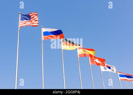 Verschiedene Länderflaggen wie Vereinigte Staaten von Amerika, Russland, Deutschland, Spanien, Schweiz, Südkorea, Thailand flattern im Wind mit blauem Himmel Stockfoto