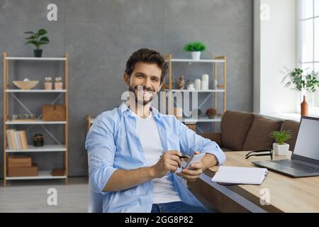 Porträt eines lächelnden Mannes, der mit einem Mobiltelefon in den Händen an einem Tisch sitzt und Notizen macht. Stockfoto