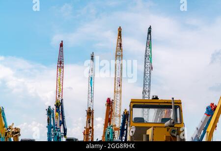 Kran gegen blauen Himmel und weiße Wolken. Immobilienbranche. Rote und gelbe Raupenkrane verwenden Aufrollvorrichtungen. Kran zur Miete auf dem Parkplatz Stockfoto