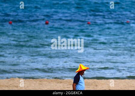 Keelung, Taipei, Taiwan. August 2021. Ein Reiniger mit Gesichtsmaske reinigt den Strand in Keelung vor der Ankunft der Strandgänger, da Taiwan laut dem taiwanesischen CDC nur 3 lokal erworbene Fälle und null Todesfälle berichtet. Die selbst regierte Insel verzeichnet seit ihrem schweren Ausbruch im Mai einen Abwärtstrend bei einheimischen Covid-Infektionen und -Todesfällen, da sie Impfstoffe für AstraZeneca, Medigen und Moderna zur Verfügung stellt, während sie Impfstoffspenden aus den USA, Japan, Litauen und der Tschechischen Republik erhalten hat, inmitten der zunehmenden militärischen Bedrohungen Chinas. (Bild: © Daniel Ceng Shou-Yi/ZUMA Press Wire) Stockfoto