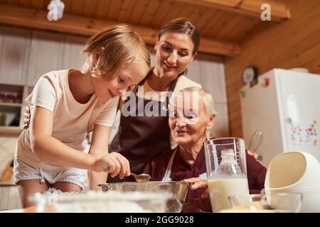 Kind hält einen Teelöffel über dem tiefen Teller, während ihre Familie zuschaut Stockfoto