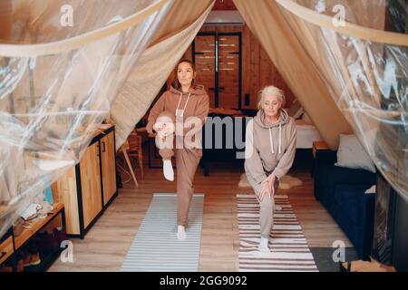 Familie macht Übungen Sport im Haus. Junge und ältere Frauen entspannen sich im Glamping-Zelt. Mutter und Tochter modernes Urlaubslebensstilkonzept Stockfoto