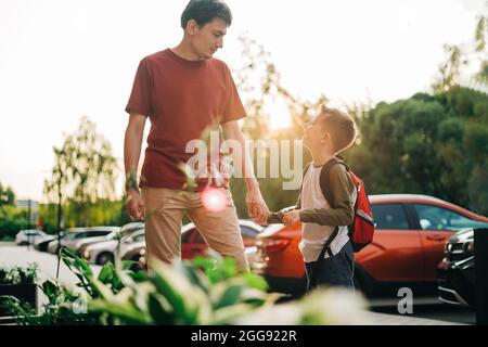 Glücklicher Vater und Kind Sohn gehen in den Unterricht. Eltern nehmen Kind Junge zur Schule in der ersten Klasse. Schüler der Grundschule gehen mit Rucksack im Freien studieren Stockfoto