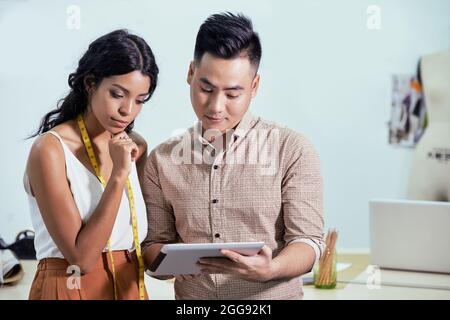 Modedesigner, der seine Ideen auf einem Tablet-Computer der nachdenklichen Näherin zeigt Stockfoto
