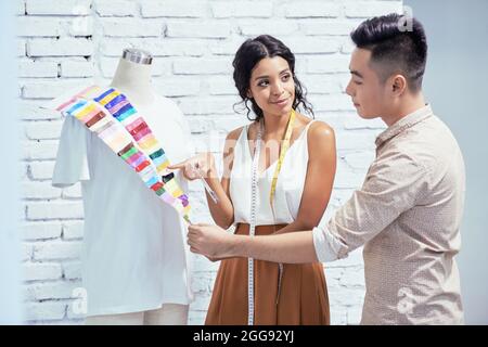 Team von jungen kreativen Modedesignern, die Stoff für die Sammlung von T-Shirts aus dem Katalog von Mustern auswählen Stockfoto