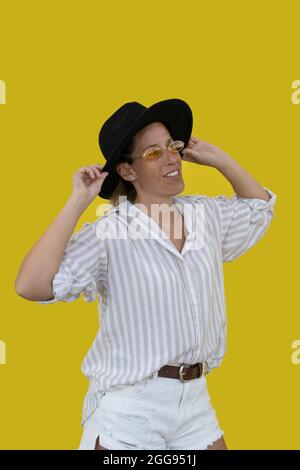 Porträt einer schönen Frau mit schwarzem Cowboy-Hut auf gelbem Hintergrund Stockfoto