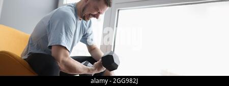 Junger Mann, der auf einem Stuhl sitzt und eine schwere Hantel hebt Stockfoto