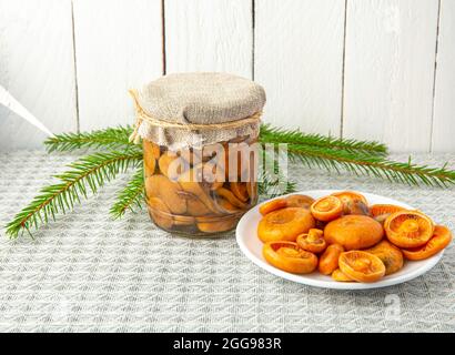 Marinierte Pilze, orangefarbene Milchkappe oder falsche Safranmilchkappe, Lactarius Deterrimus im Glasgefäß und frisch gepflückte Pilze auf dem Teller. Stockfoto