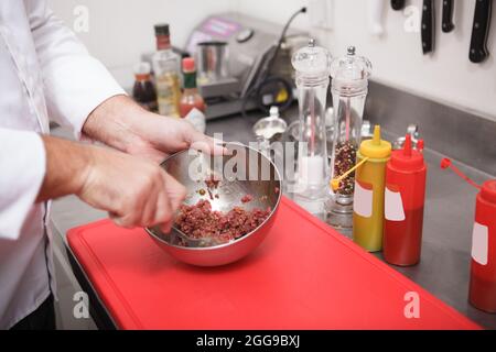 Nahaufnahme der Hände des Küchenchefs, die in einer Metallschüssel gehacktes Rindfleisch für Tartar rühren Stockfoto