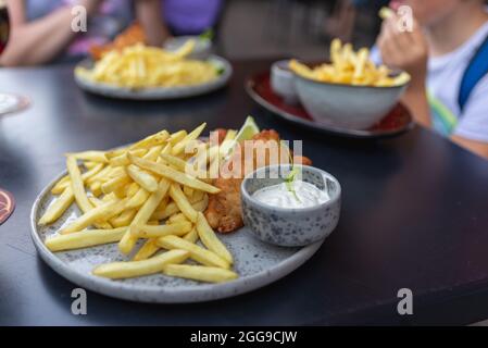 Mittagessen mit Fisch in Semmelbröseln und Teig, pommes Frites, Kartoffeln, Tartarsauce für Fisch. Pommes Frites und Thymian. Unscharfer Hintergrund im Freien. Stockfoto