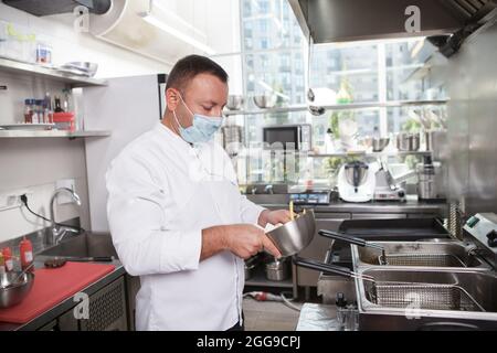 Chefkoch mit medizinischer Gesichtsmaske bei der Arbeit in der Restaurantküche, Platz kopieren Stockfoto