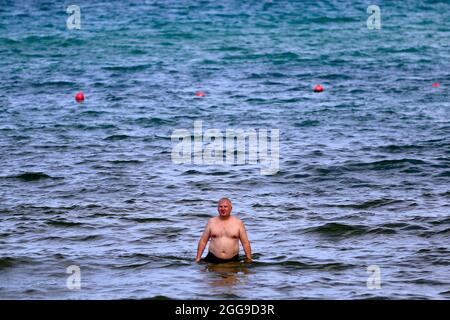 Keelung, Taipei, Taiwan. August 2021. Ein Ausländer wird im Ozean in der Nähe eines Strandes in Keelung gesehen, wo die Menschenmenge kontrolliert wird, da Taiwan laut dem taiwanesischen CDC nur 3 lokal erworbene Fälle und null Todesfälle meldet. Nachdem die Versammlungen und Schwimmaktivitäten wieder aufgenommen wurden, verzeichnet die selbstregierte Insel seit ihrem schweren Ausbruch im Mai einen Abwärtstrend bei einheimischen Covid-Infektionen und -Todesfällen, indem sie Impfstoffe für AstraZeneca, Medigen und Moderna zur Verfügung stellt, während sie Impfstoffspenden aus den USA, Japan, Litauen und der Tschechischen Republik erhält. Angesichts der zunehmenden militärischen Bedrohungen Chinas. (Credi Stockfoto