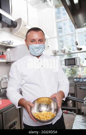Vertikale Aufnahme eines professionellen Küchenchefs mit medizinischem Gesicht, msk, der eine Schüssel mit pommes Frites hält Stockfoto